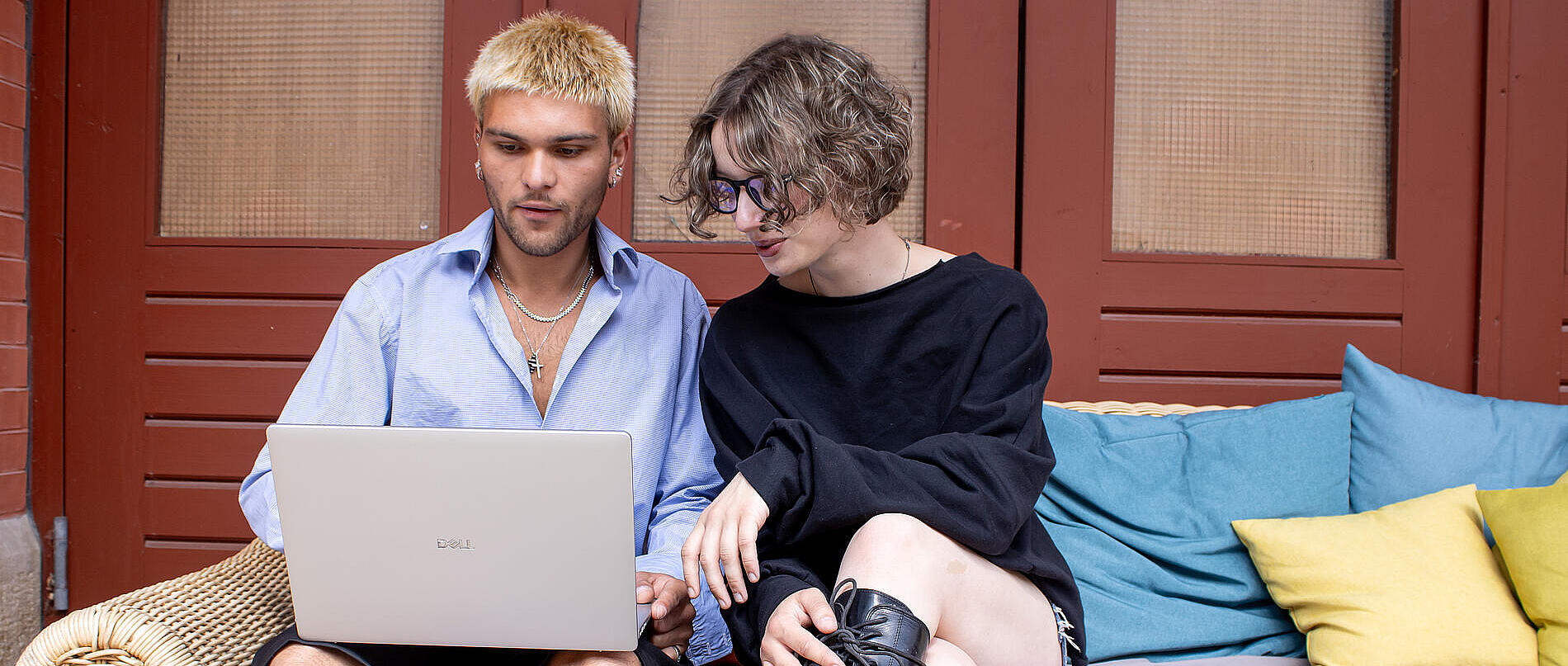 Zwei Personen sitzen auf einer Couch und arbeiten gemeinsam an einem Laptop