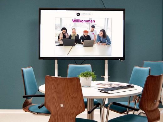 Gebäude 2 In der Au - Moderner Meetingraum mit großem ovalen Tisch mit Stühlen und einem Digitalboard.