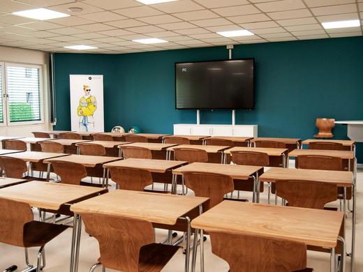 Gebäude 2 In der Au - Großer Unterrichtsraum mit modernem Digitalboard, Tischen und Stühlen.