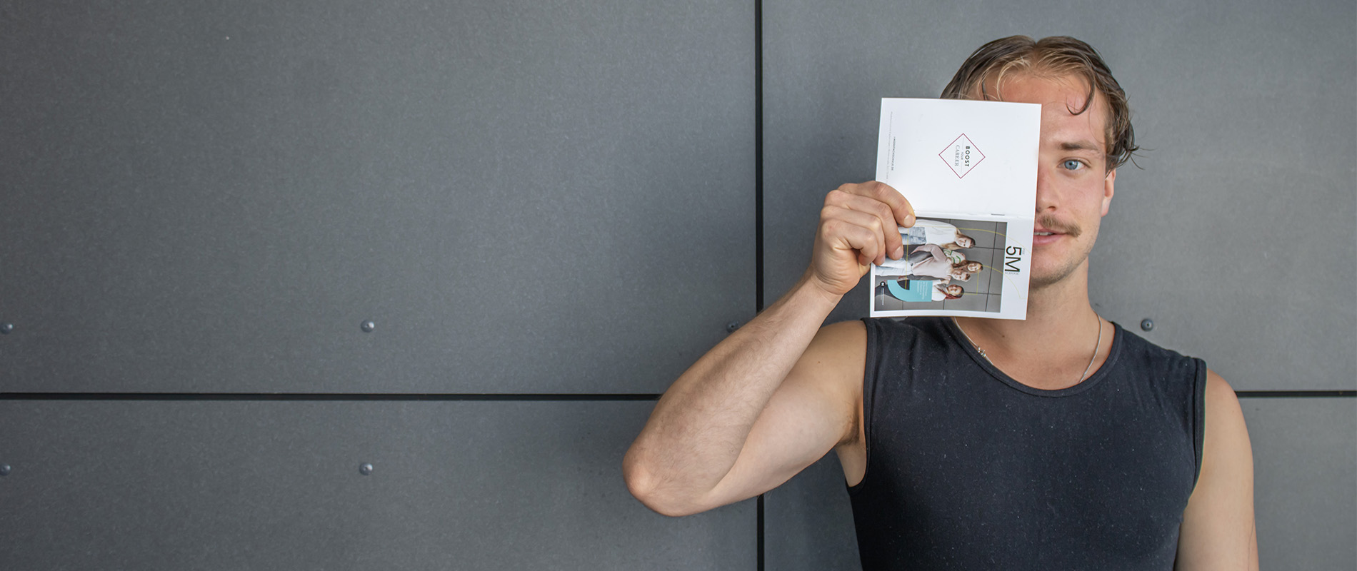 junger Mann mit Infobroschüre vor dem Gesicht